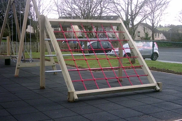 An A-frame timber assault net with a red rope net and a ladder, installed on a black rubber tile safety surface in a school playground.