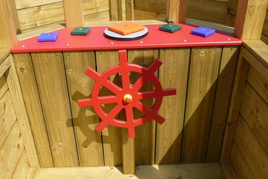 A close-up of the red ship's wheel and interactive play panel on the Boat Stage.