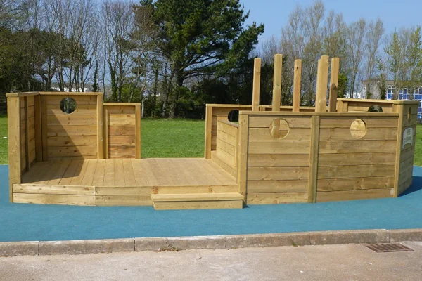 A full side view of the large wooden Boat Stage play ship on a blue safety surface in a school playground.