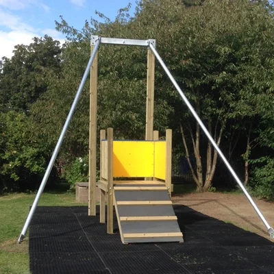 A Cableway zip wire with a wooden launch platform, yellow safety panel, and galvanised steel frame, installed on a rubber safety surface in a garden playground.