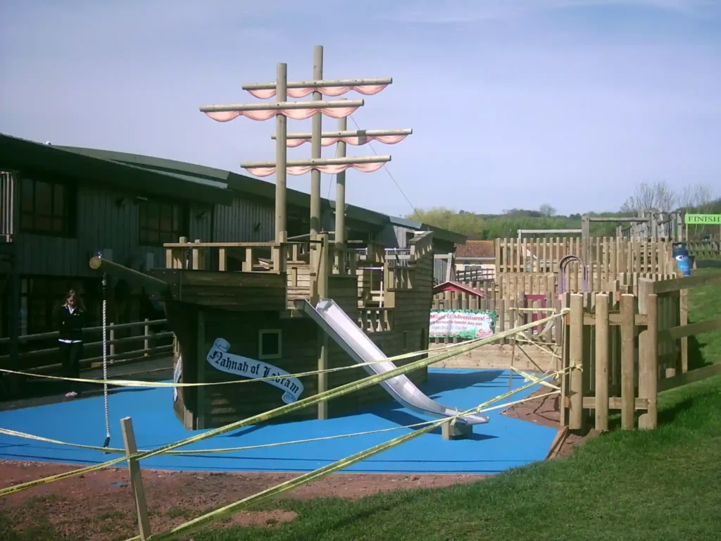 The Coverack Queen, a large wooden pirate ship outdoor play equipment with a slide, in a playground setting.