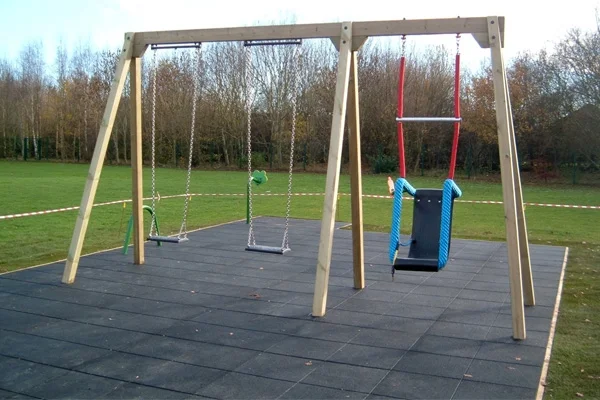 A rear view of a timber double bay triple swing with an inclusive seat and two flat seats, on a black rubber tile surface in a park setting.