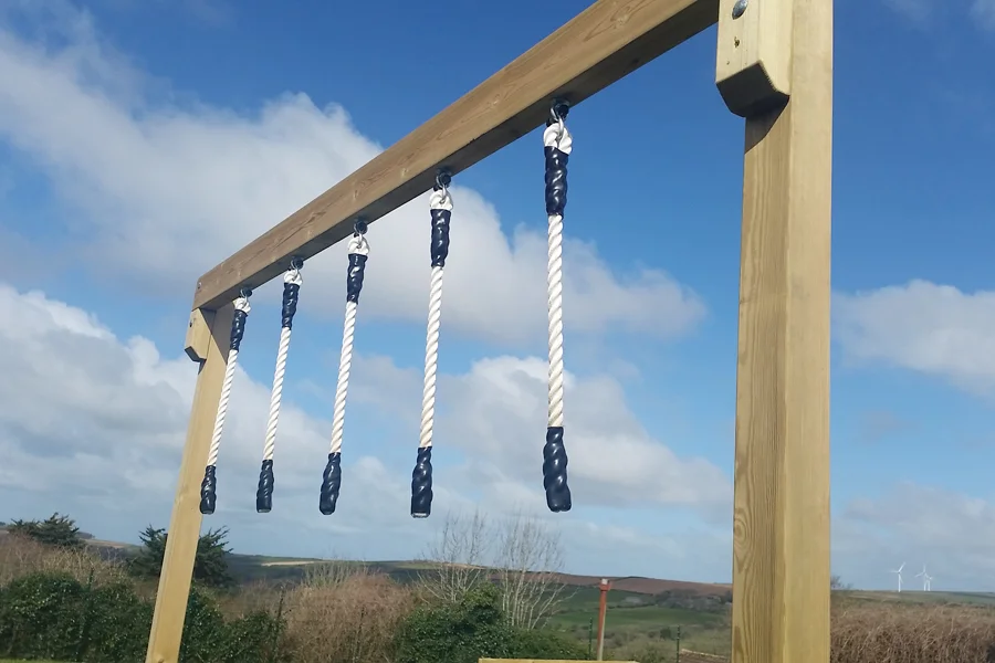 A close-up of Drop Rope Traverse hanging ropes with navy blue rubber handles against a bright blue sky and rolling hills.