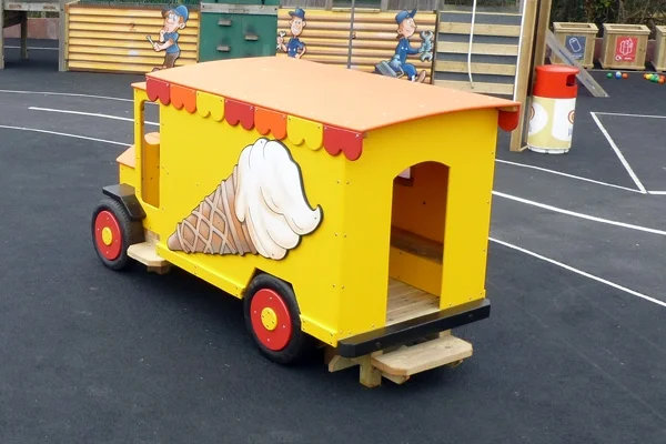 A side view of a yellow and orange timber play ice cream van with an ice cream cone artwork, on a rubber surface in an outdoor playground.