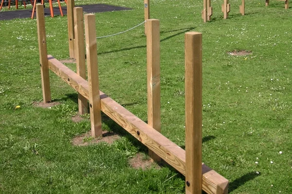 An inclined wooden Post Weave outdoor play equipment on a grassy school field, forming part of a trim trail.