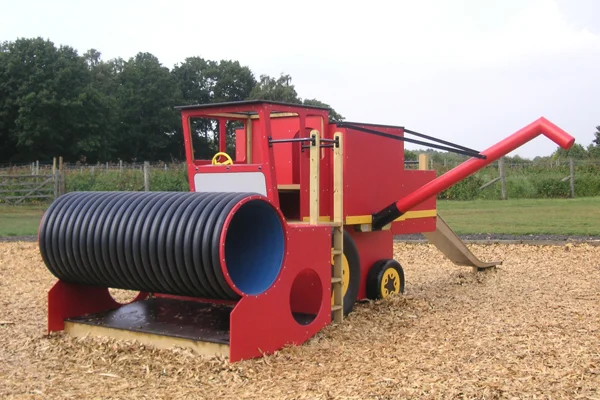 A red timber play combine harvester with a black corrugated tube slide, in a woodchip outdoor playground.