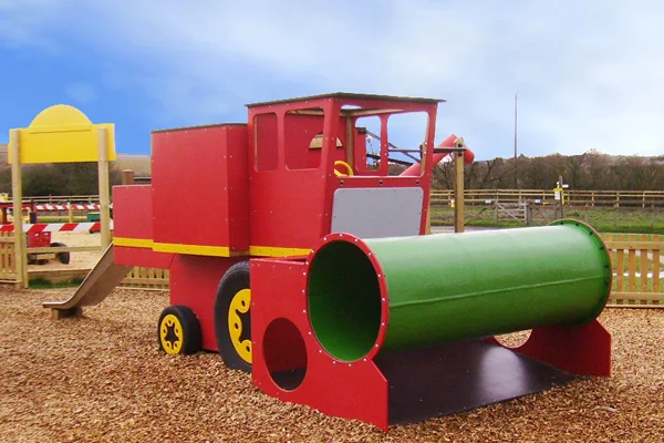 A red and yellow timber play combine harvester with a green tube, in a woodchip outdoor playground.