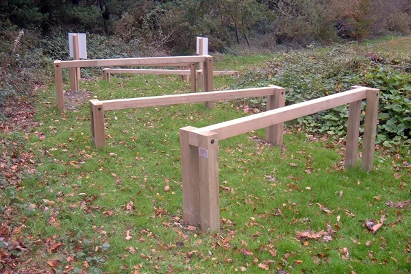 A series of wooden Leaping Bars set up as a trim trail in an autumn woodland setting with fallen leaves on the ground.