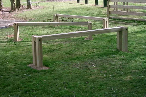 A set of three wooden Leaping Bars of different heights, installed as hurdles in a grassy park setting.
