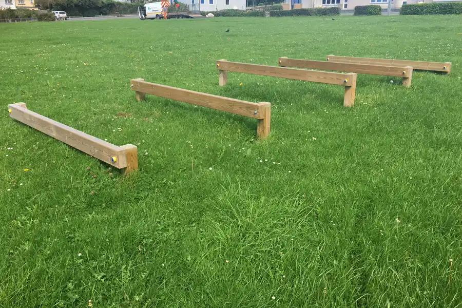 A line of four low-level wooden Leaping Bars installed as a trim trail in a large, green school playing field.