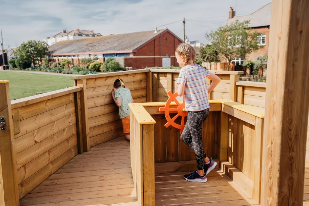 Child using steering wheel on Martha D wooden playground boat
