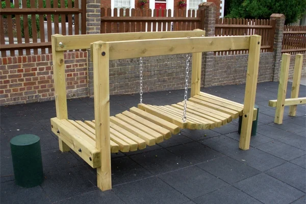 The Mini Wobbly Bridge outdoor play equipment, showing its wooden frame and chain-suspended walkway on a rubber tile surface.