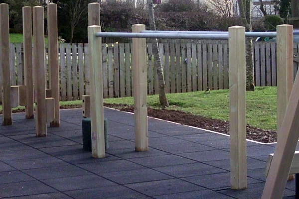 A set of wooden and metal Parallel Bars installed on a black rubber tile safety surface in a playground.