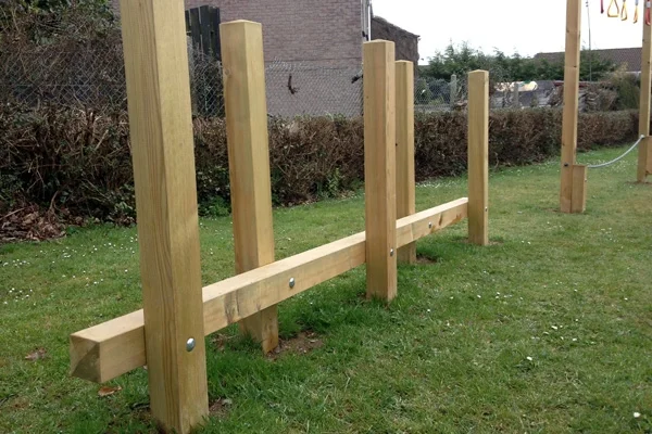 A sturdy wooden Post Weave outdoor play equipment with a balance beam and vertical posts, set in a grassy playground.