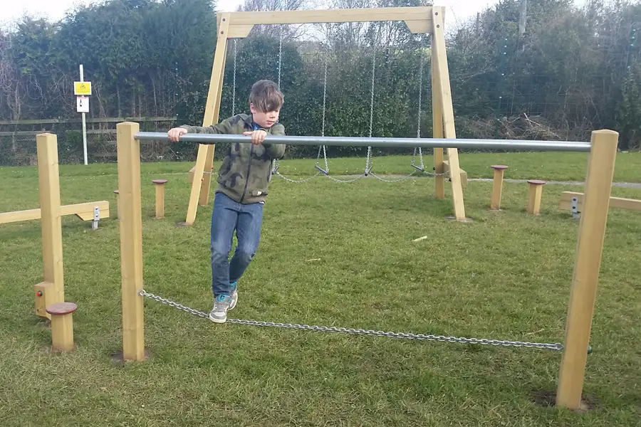A child steps onto the chain of the Postman's Bridge, with swings and other play equipment in the background.