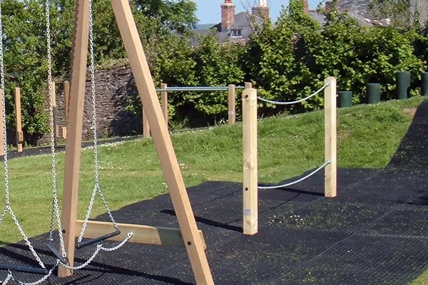 The Postman's Bridge outdoor play equipment, featuring a chain balance beam and metal handrail, on a rubber safety surface.