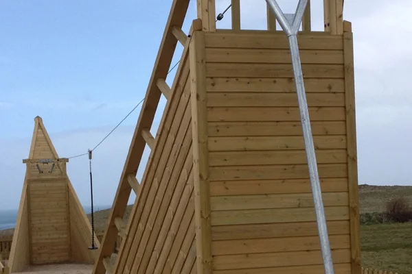 A close-up of the tall wooden Shipwreck Cableway zip wire tower showing the launch platform, angled support struts, and zip wire cable stretching to a second tower in the background.