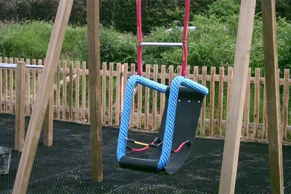 A close-up of a special needs cradle swing, showing the black rubber seat, blue rope surround, and red hangers on a timber A-frame over a rubber mat.