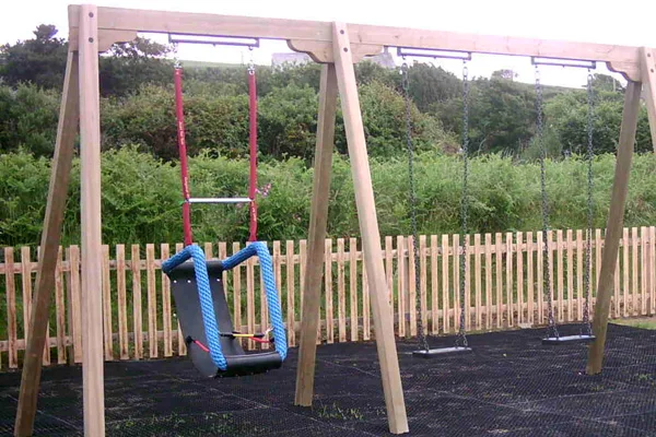 A special needs cradle swing with a black seat and blue rope surround, installed on a timber triple swing frame alongside two standard swings in an outdoor playground.