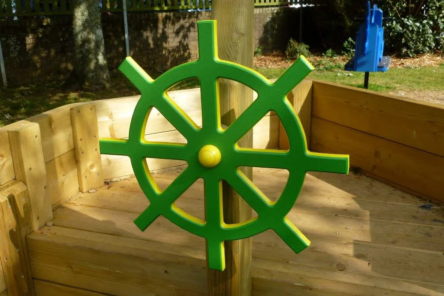 A close-up of a bright green ship's wheel on the St Columb Sailor wooden outdoor play boat.