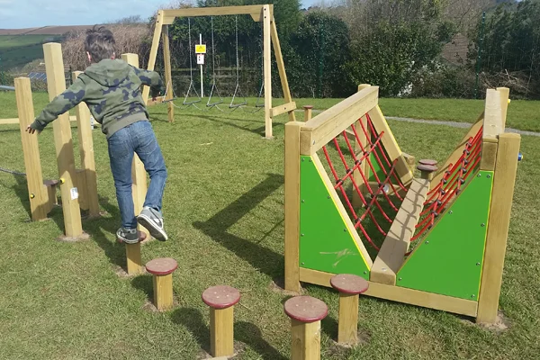 A boy in a camouflage top balancing on a set of Stepping Logs, part of an outdoor trim trail in a park.