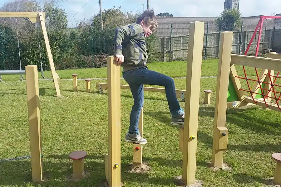 A young boy in a camouflage hoodie climbing on the wooden Stepping Stilts as part of an outdoor trim trail.