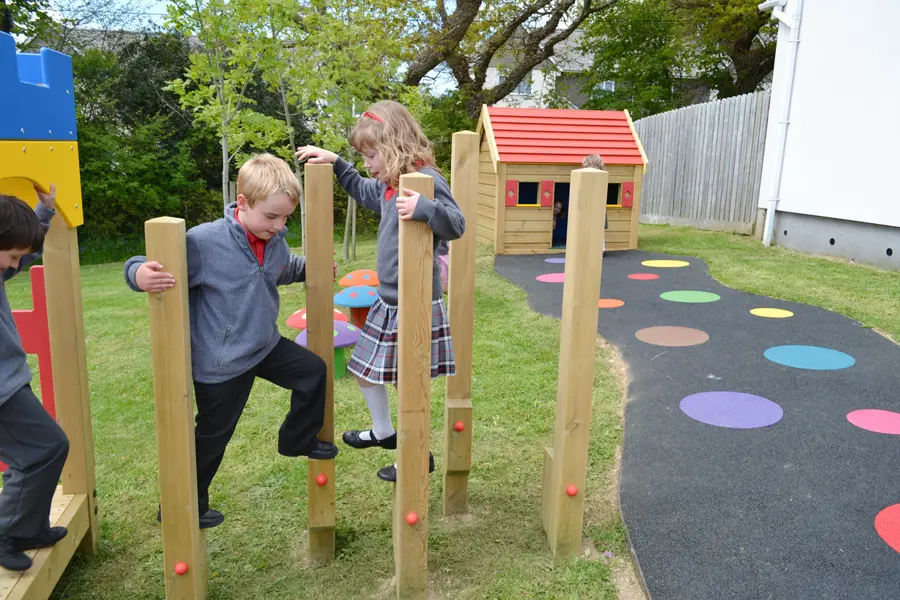 Two school children in uniform playing together on the wooden Stepping Stilts in a colourful school playground.