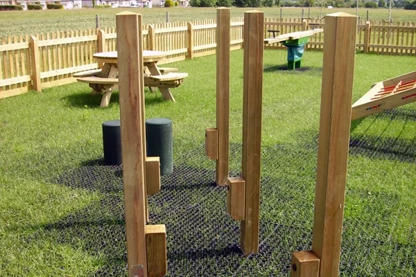 A set of wooden Stepping Stilts outdoor play equipment installed on a black rubber grass mat safety surface.