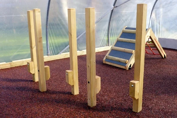 A set of wooden Stepping Stilts in an indoor play area, with a climbing ramp in the background.