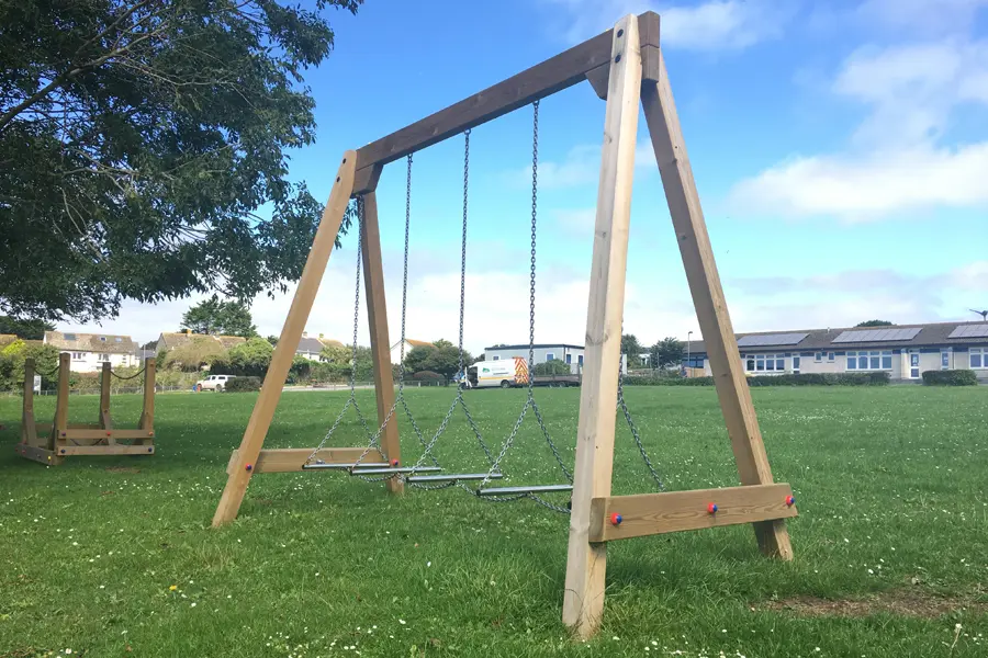 A wooden A-frame Swinging Steps with chain balance steps, located in a grassy park playground.