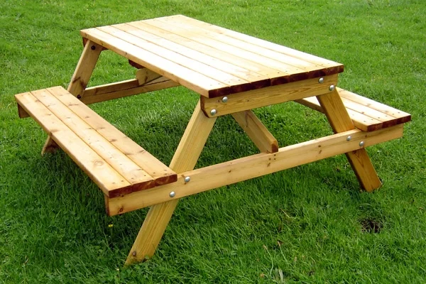 A newly-made timber picnic bench with a natural wood finish, shown from an angle on a lush green lawn, ideal for outdoor seating.