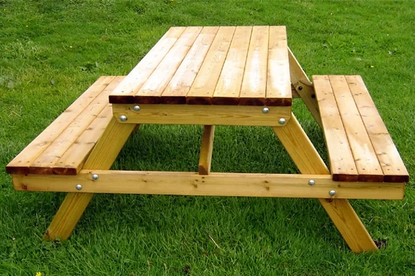 A top-down view of a timber picnic bench, showing the slatted tabletop and attached benches, set on a bright green grassy lawn.