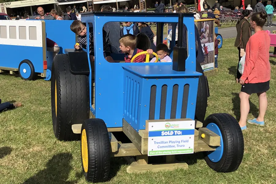 A blue timber play tractor with children inside, at an outdoor show.