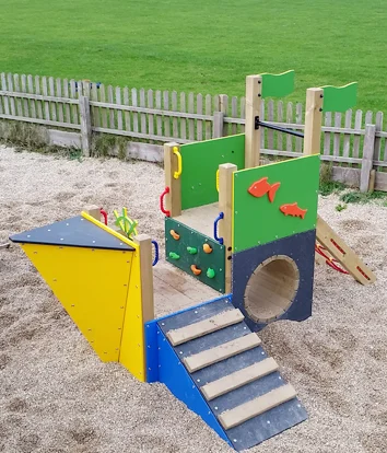 A colorful Trenance Trawler children's outdoor play boat with a climbing frame, set in a sandpit.