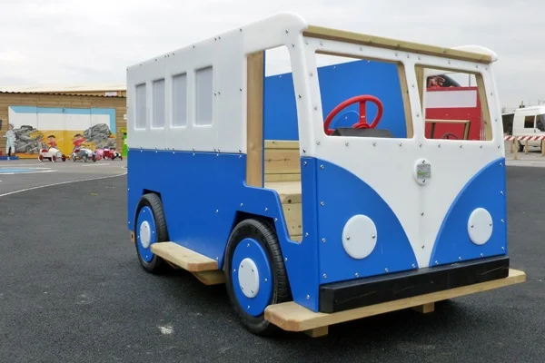 A front-quarter view of a blue and white Veedub camper van slide, showing the interior with a red steering wheel.