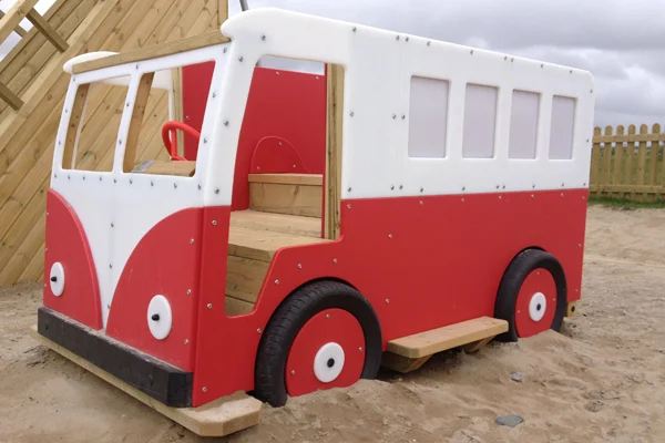 A front-quarter view of a red and white Veedub camper van slide play structure, situated in a sandpit.
