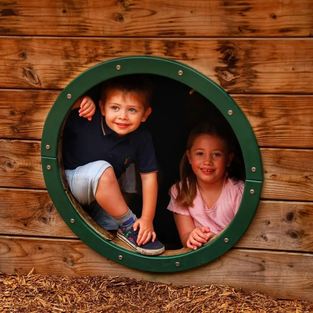 Children looking through porthole window on timber pirate ship playground
