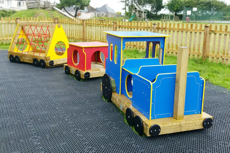 Colorful wooden toy train with blue, red, and yellow carriages on a playground with grass and wooden fence