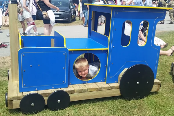 Colorful wooden toy train with blue, red, and yellow carriages on a playground with grass and wooden fence