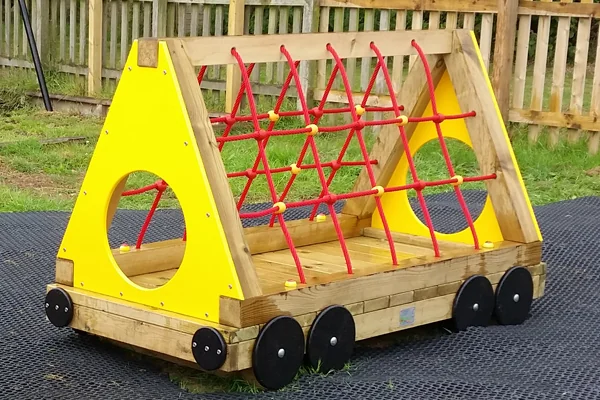 Wooden triangular climbing frame with red rope netting and yellow panels on black rubber matting outdoors near a wooden fence