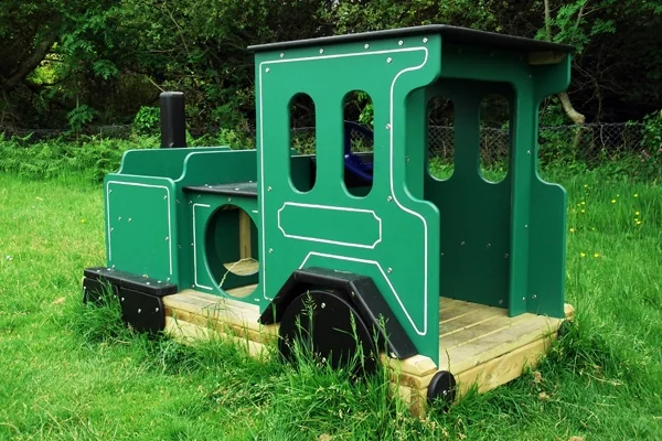 Green and black wooden miniature train engine on grass with trees in background