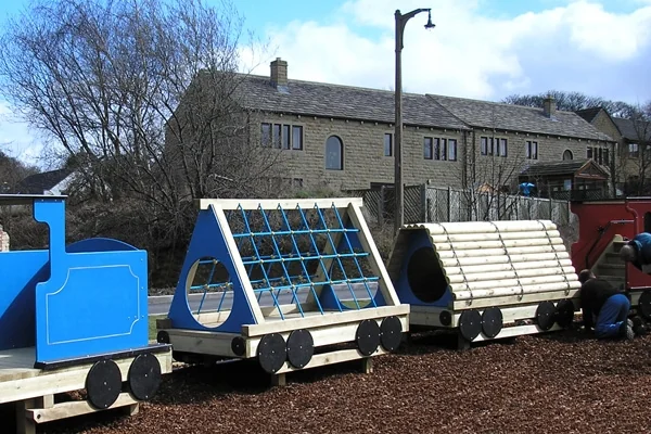 Colorful wooden miniature train with blue and natural wood cars on outdoor playground with buildings and trees in background