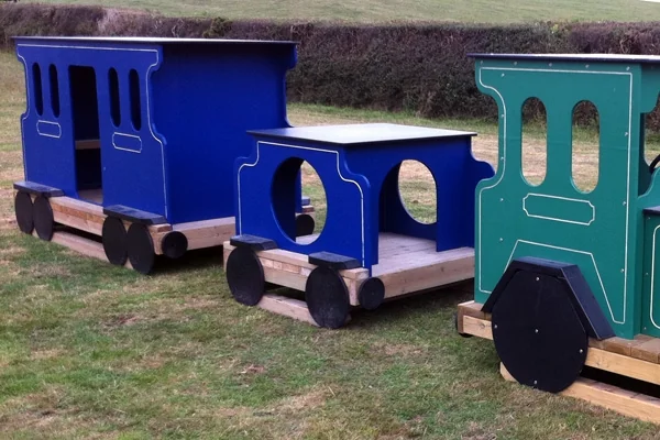 Colorful wooden miniature train cars in blue and green on grass outdoors with hedge background