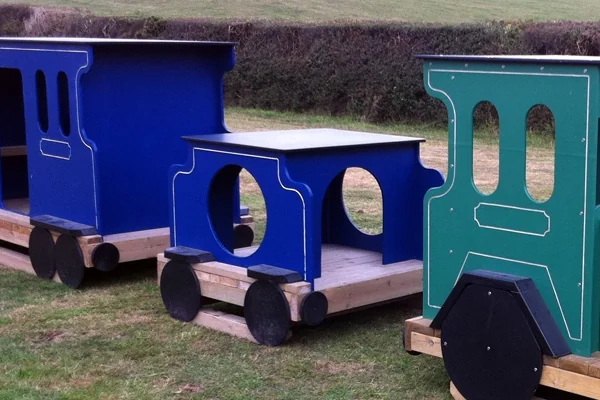 Colorful wooden miniature train with blue and green carriages on grass outdoors near a hedge