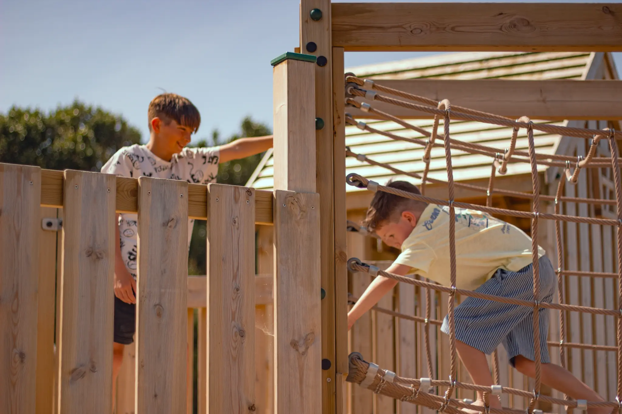 Two boys exploring a timber play frame at Padstow, with rope-net climbing and vertical timber panels.